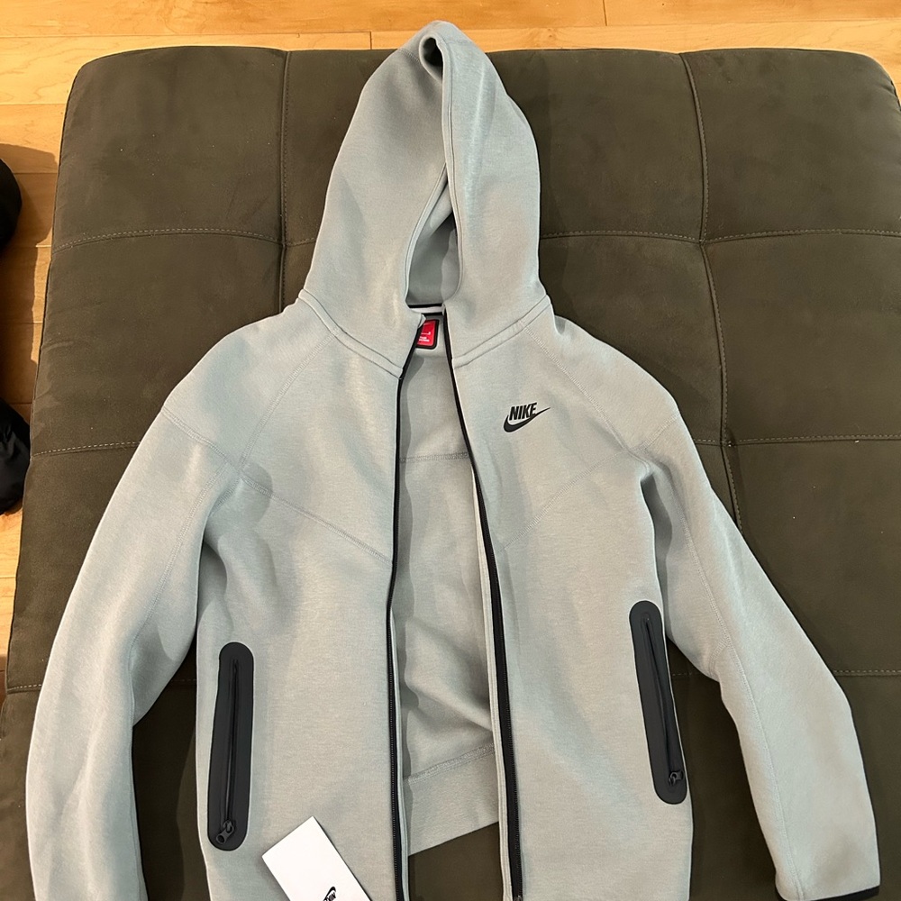 New With Tags. Nike Gray Jacket with Black Details, Hood, and Zippered pockets.